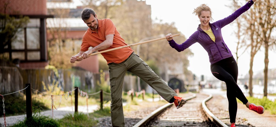 Mann und Frau balancieren mit Stock auf stillgelegtem Bahngleis