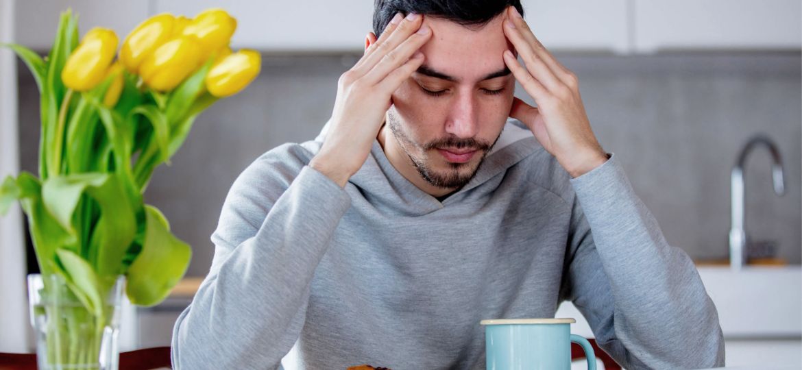Mann hat Kopfschmerzen, sitzt an Tisch mit Tulpen im Vordergrund