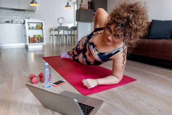 Frau macht Sportübung auf Matte daheim mit Hilfe von Laptop