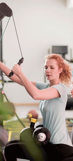Eine Therapeutin unterstützt eine Frau beim Training an einem Sportgerät